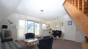 A cozy living room with a sofa, two armchairs, a small table, and a kitchen area with a dining table and chairs.