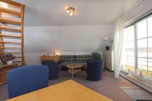 A living room with a wooden bookshelf, a sofa, two armchairs, a small round table, and a television. - Morgensonne Apartment - Apartment in a quiet location with a balcony - (Breege)
