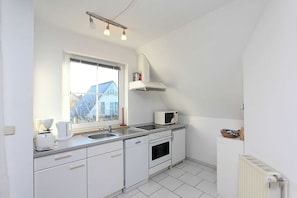 A compact kitchen with white cabinets, a built-in oven, a microwave, and a window overlooking a residential area. - Morgensonne Apartment - Apartment in a quiet location with a balcony - (Breege)