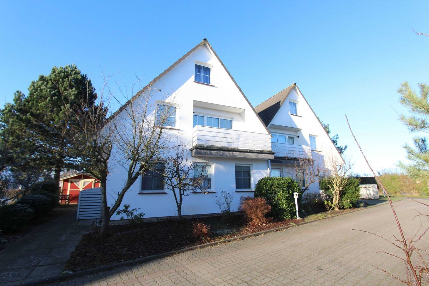 A two-story residential building with a sloped roof, a balcony on the upper floor, and a small attached garage.