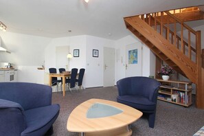 Ein Wohnzimmer mit Holzboden, einer Essecke mit Tisch und Stühlen sowie einem Bücherregal mit Büchern und einem Blumentopf.