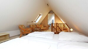 A bedroom with a sloped ceiling, a bed with white linens, a wooden staircase, and a seating area with wicker chairs.