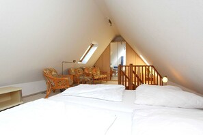 A bedroom with a sloped ceiling, a bed with white linens, a wooden staircase, and a seating area with wicker chairs. - Apartment Morgensonne - Apartment in a quiet location with balcony - (Breege)