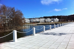 A waterfront promenade with a chain barrier, a river, and a row of white buildings in the background.