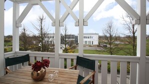 A covered outdoor seating area with a table and chairs, a vase with flowers, and a view of a building and trees.