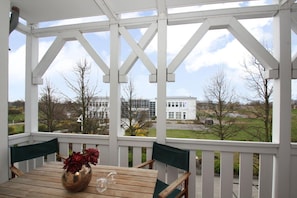 Un espace extérieur aménagé avec une zone de sièges couverte, comprenant une table et des chaises, un vase avec des fleurs et une vue sur un bâtiment et des arbres.