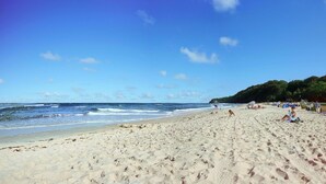 A wide sandy beach with ocean waves, tents, and people.