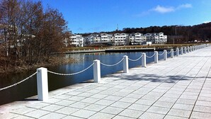 A waterfront promenade with a chain barrier, a river, and a row of white buildings in the background.