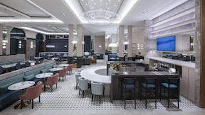 Um lobby de hotel moderno com área de bar, assentos e um grande candelabro.