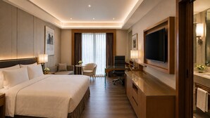 Quarto de hotel com uma cama grande, uma escrivaninha, uma televisão e um banheiro com espelho e porta-toalhas.