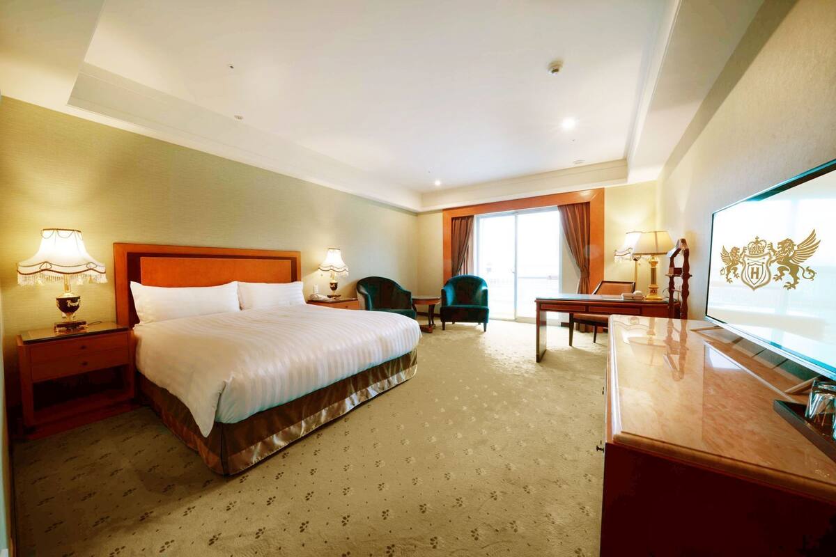 A hotel room with a large bed, a desk, a chair, a television, and a window with curtains.