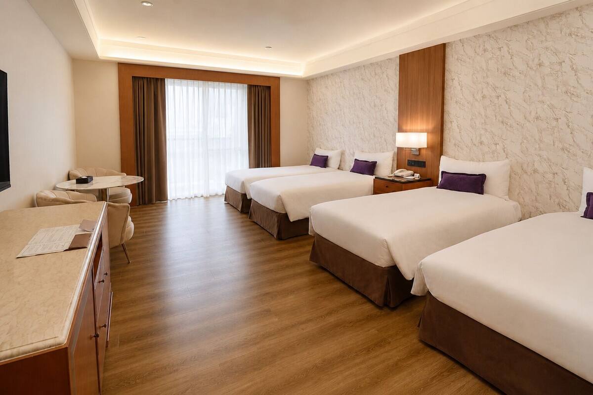 A hotel room with two beds, a desk, a chair, a small table, and a large window with curtains.