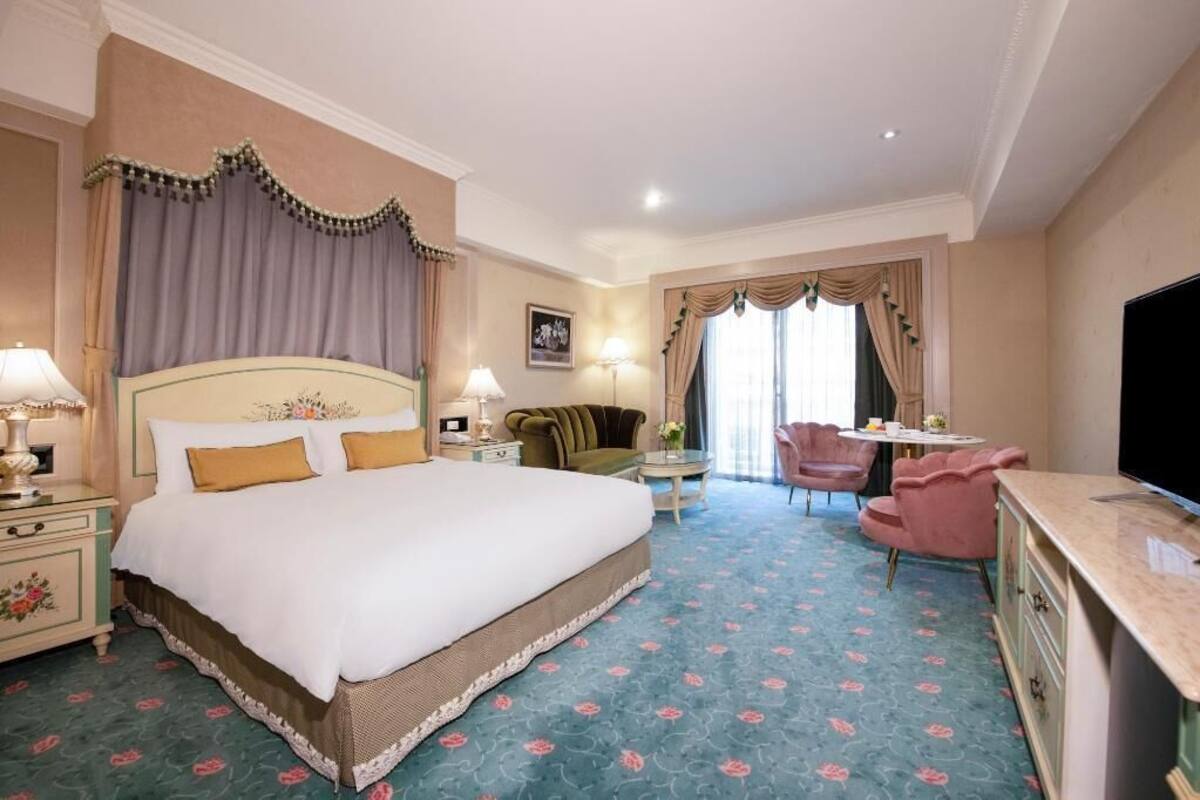 A hotel room with a large bed, a desk, a chair, and a television.