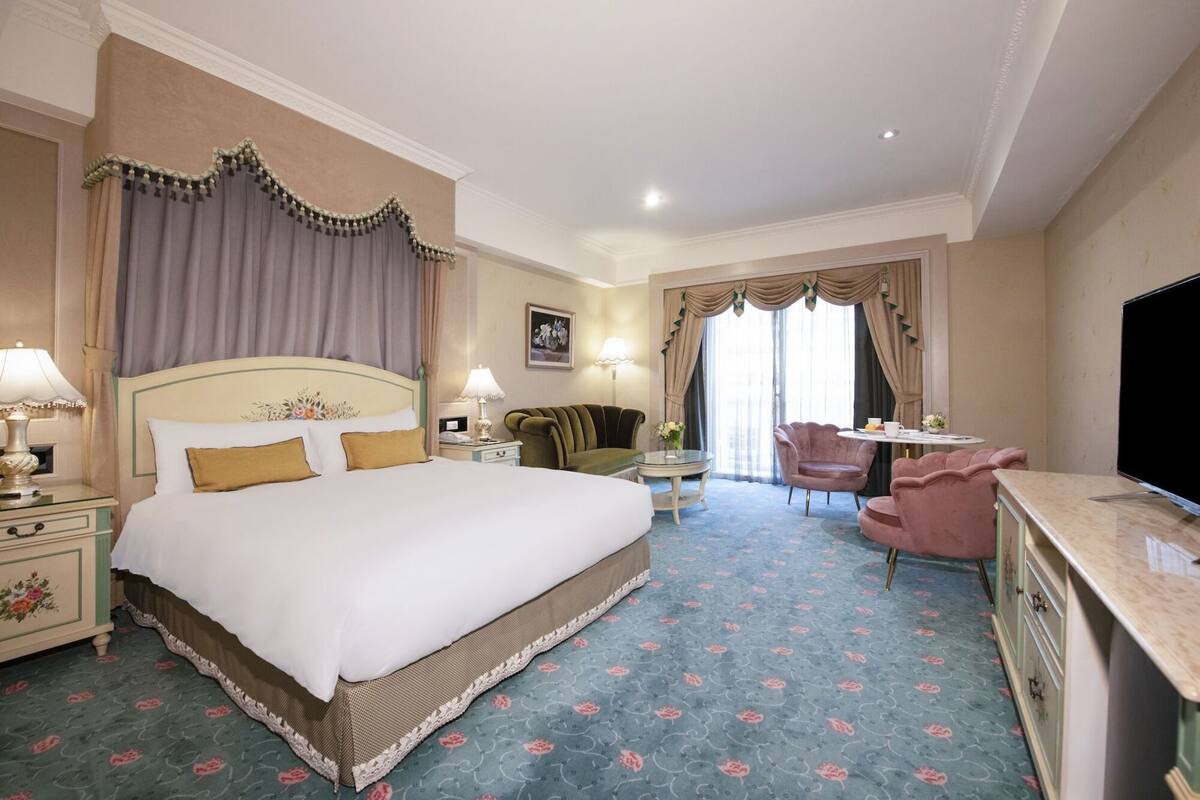 A hotel room with a large bed, a desk, a chair, and a television.