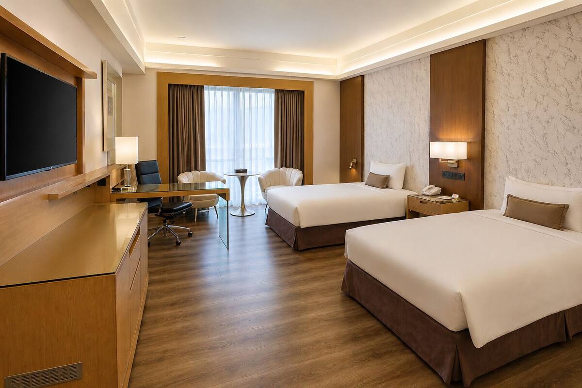 A hotel room with two beds, a desk, a chair, a TV, and a small table.
