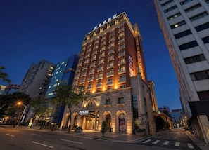 Un hotel moderno de gran altura con múltiples pisos, amplias ventanas y una entrada destacada con diseño en arco.