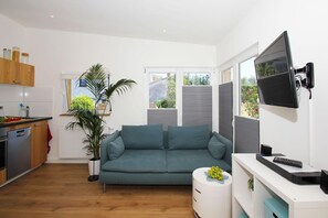 A modern living space with a kitchen, a sofa, a TV, and a small side table with a remote control. - Villa Elise F-1093 Apartment 01 - F-1093 Villa Elise (Göhren)