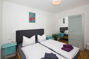 A modern hotel room with a large bed, a mirror, a small desk, and a potted plant.