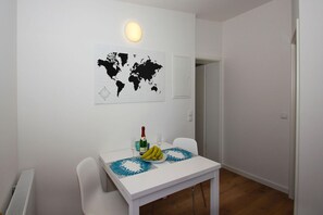 A dining area with a white table, two chairs, a world map, a bottle of champagne, and a plate of bananas.