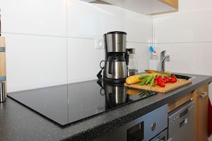 A kitchen with a black countertop, a coffee maker, a cutting board with vegetables, and a sink.