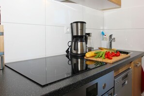 Une cuisine avec un plan de travail noir, une machine à café, une planche à découper avec des légumes et un évier.