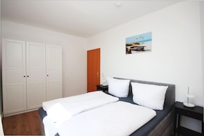 A bedroom with a bed, a nightstand, a wooden door, and a wall-mounted picture. - Villa Elise F-1093 Apartment 02 - F-1093 Villa Elise (Göhren)