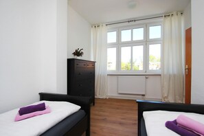 A room with two beds, a dresser, a radiator, and a window with curtains. - Villa Elise F-1093 Apartment 02 - F-1093 Villa Elise (Göhren)