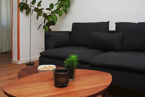 A modern living room with a dark grey sofa, a small round wooden table, a potted plant, and a bowl of snacks. - Villa Elise F-1093 Apartment 02 - F-1093 Villa Elise (Göhren)