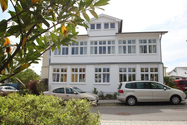 A two-story residential building with a symmetrical facade, multiple windows, and a parked car in front.