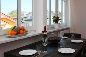 Un comedor con una mesa dispuesta para dos, una botella de champán y un frutero en el alféizar.