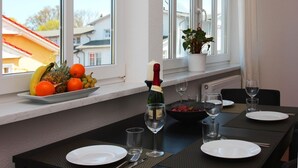 Uma área de refeições com uma mesa posta para dois, uma garrafa de champanhe e uma cesta de frutas no parapeito da janela.