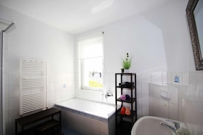 A bathroom with a bathtub, a window, a shelf with towels, and a radiator.