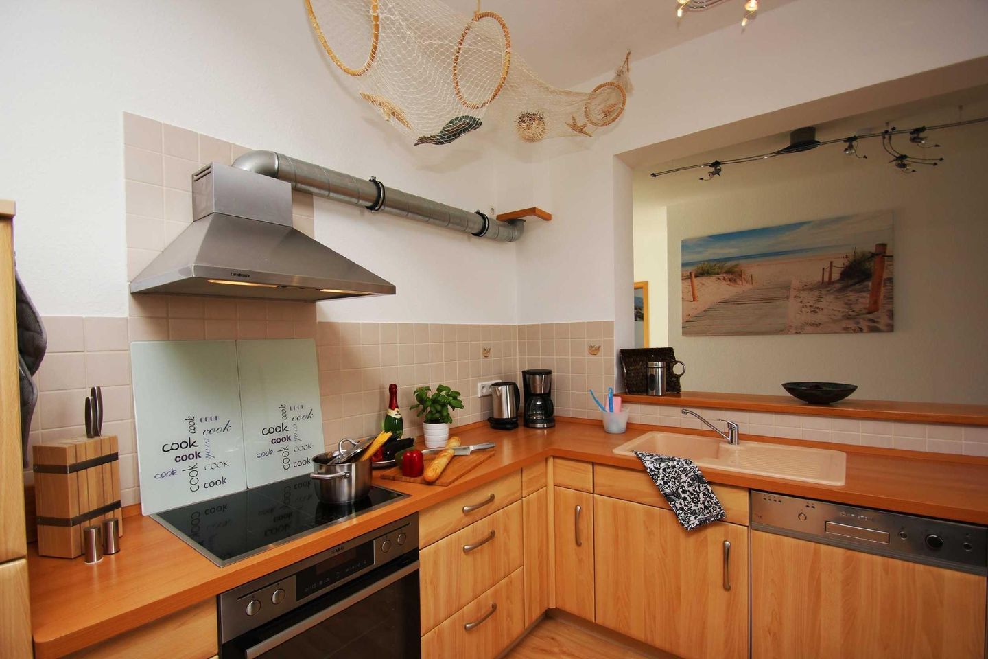 A modern kitchen with wooden cabinets, a stainless steel range hood, a black induction cooktop, and a dishwasher.