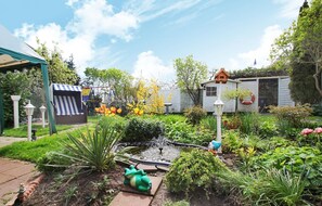 Un jardín con un estanque, un pequeño puente y una gran variedad de plantas y flores.