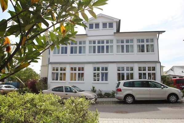 A two-story residential building with a symmetrical facade, multiple windows, and a parked car in front.
