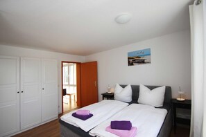 Een slaapkamer met twee bedden, een houten deur, een klein tafeltje met een lamp en een foto aan de muur.