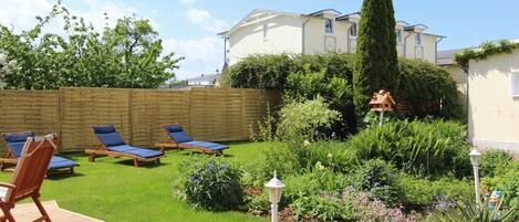 A backyard with a wooden deck, lounge chairs, and a garden with various plants and flowers.