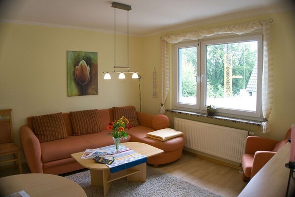 A cozy living room with a sofa, a coffee table, and a window with curtains.