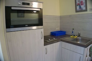 Una kitchenette con horno empotrado, un lavamanos y una cesta azul para guardar objetos.