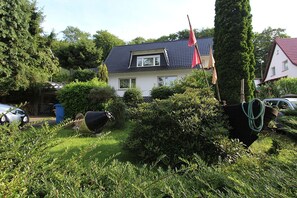 Una casa con techo inclinado, rodeada de setos cuidados y un árbol grande.