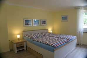 Cama de casal com roupa de cama listrada, mesas de cabeceira com abajures e quadros nas paredes.