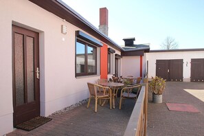 Un edificio con puerta de vidrio, ventana y patio de ladrillo con mobiliario exterior.