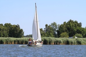 Un velero en un río tranquilo con una orilla boscosa al fondo.