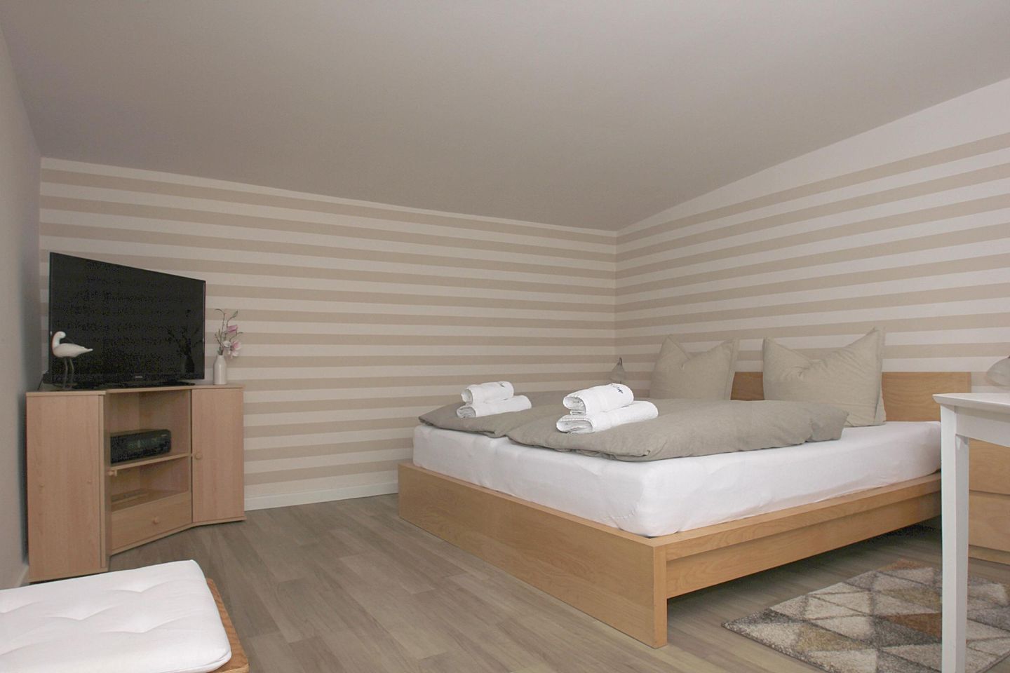 Une chambre à coucher bien rangée, avec un lit, un téléviseur posé sur un meuble, une petite armoire et une table de chevet.