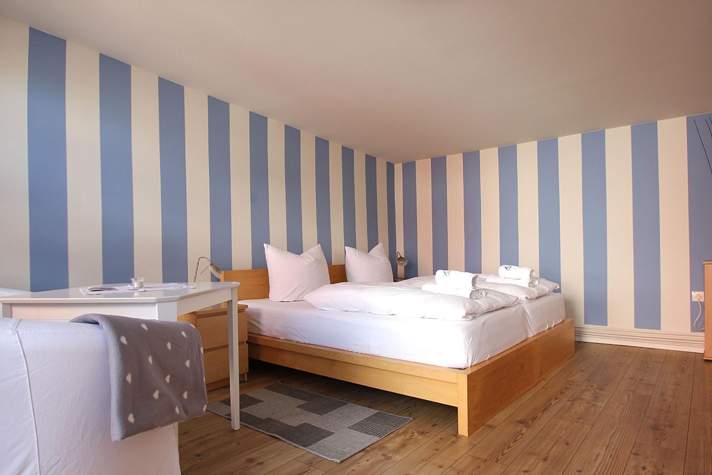 A bedroom with a wooden bed, a bedside table, a chair, and a striped wall.