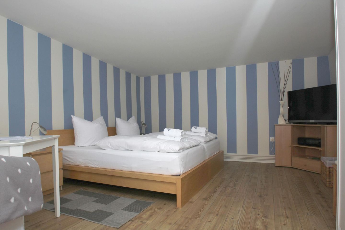 A bedroom with a bed, bedside table, TV, and a wooden floor.