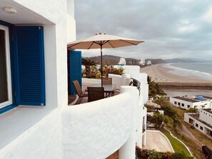Enjoy the ocean view from this balcony with a table and chairs, shaded by a large umbrella.