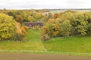 En lantlig fastighet med ett stort hus omgivet av träd och åkrar.