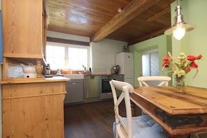 Una cocina con armarios de madera, una mesa de comedor y sillas. Hay un florero con flores sobre la mesa.