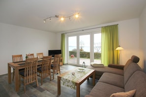 Ein Wohnzimmer mit einem Holzesstisch, Stühlen, einem Sofa und einem Fernseher.